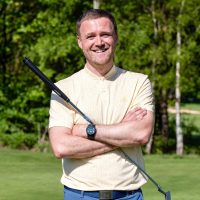 Male holding golf club next to golf flag on the golf course.
